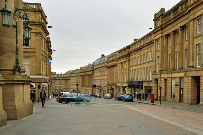 Cars on street by buildings against sky in city