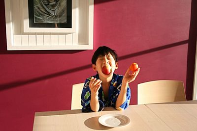 Portrait of boy sitting on table against wall