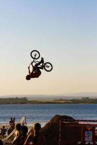 Man with bicycle jumping over sea against clear sky