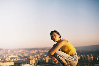 Side view portrait of woman crouching against cityscape