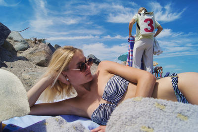 Young woman wearing bikini while lying at beach against sky