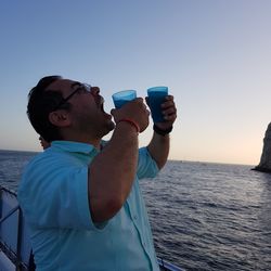 Man drinking water against sea during sunset