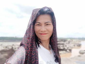 Portrait of smiling young woman standing on beach against sky