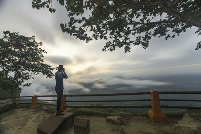 Man standing by railing against sky