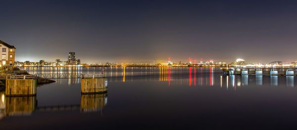 Illuminated bridge over river against sky at sunset