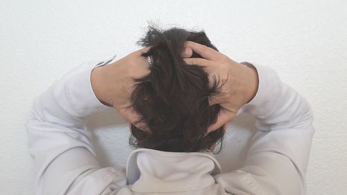 Rear view of woman with hands in hair towards wall at home