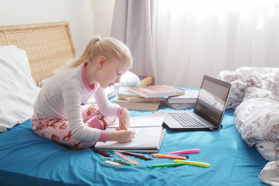 Cute girl studying while sitting on bed at home