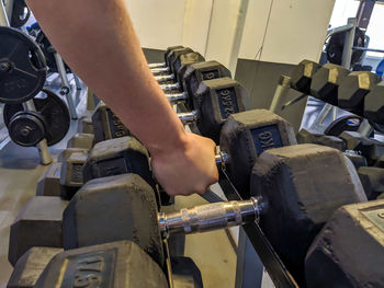 Midsection of man holding dumbbell while standing in gym