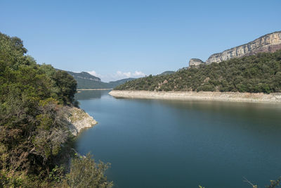 Scenic view of river by mountains against clear blue sky