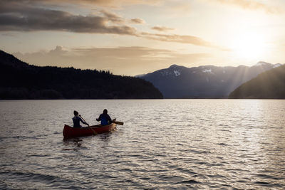 People on boat in lake against sky during sunset