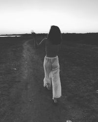 Rear view of woman walking on field against sky