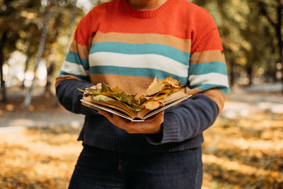 Faceless plus size woman with book and maple leaves in fall autumn park in sun lights. body positive