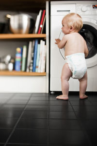 Baby boy wearing diaper standing in kitchen