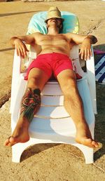 Full length of shirtless man resting on chair at beach