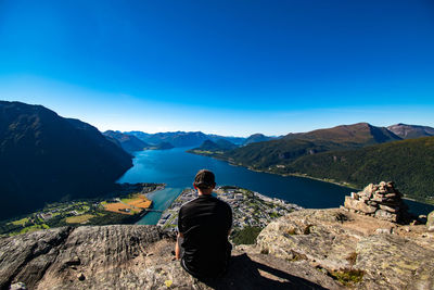Rear view of man sitting on mountain against clear blue sky