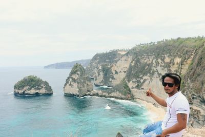 Portrait of young man gesturing sitting by cliff