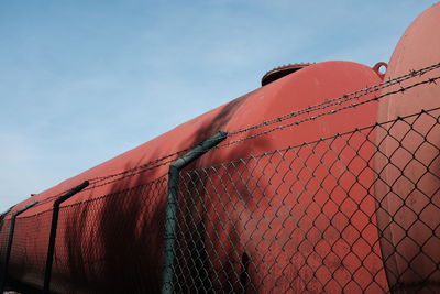 Low angle view of chainlink fence by metallic tanks against sky