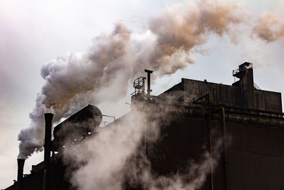 Smoke emitting from factory against sky