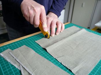 Midsection of craftsman using rotary cutter on fabric in workshop