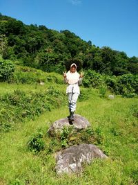 Woman gesturing peace sign while standing on rock amidst grassy field