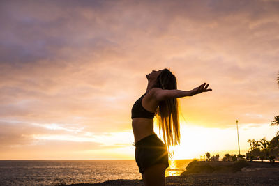 Side view of woman standing by sea against sky during sunset