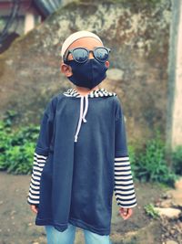 Cute boy wearing mask and sunglasses standing outdoors