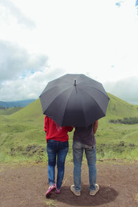 Rear view of couple standing with umbrella against sky