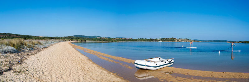 Inflatable boat moored on lakeshore against clear blue sky