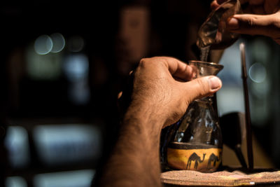 Cropped hands of man pouring sand in bottle on table