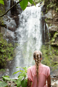 Rear view of woman standing against waterfall