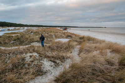 Rear view of woman walking on beach against sky