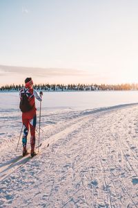 Rear view of person on snow covered field against sky during sunset