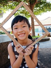 Portrait of smiling girl holding frame outdoors