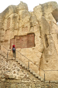 Visitor on the staircase impressed by armenian cross-stones on the cliff wall, geghard monastery