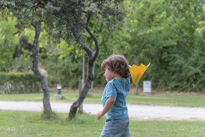 Happy kid playing with toy airplane against summer sky background at sunset.