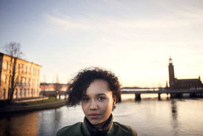 Portrait of teenage girl with curly short hair standing against canal in city