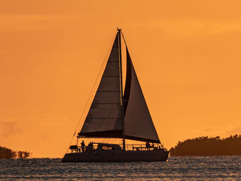 Silhouette sailboat sailing on sea against orange sky