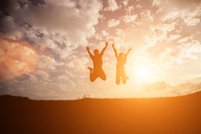 Silhouette woman with arms raised against sky during sunset