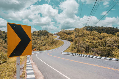 Road sign by trees against sky