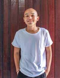 Portrait of smiling boy standing against wooden wall