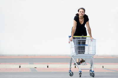 Full length portrait of smiling woman standing on shopping cart