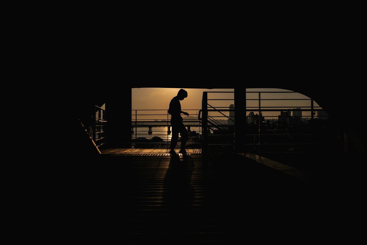 REAR VIEW OF SILHOUETTE MAN WALKING ON STEPS AGAINST SKY