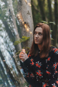 Young woman standing by tree trunk