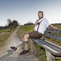 Portrait of man sitting on bench against clear sky