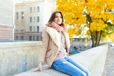 Woman sitting on wall in city during autumn