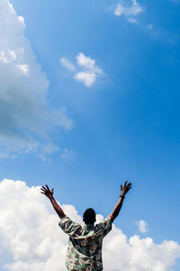 Low angle view of man with arms raised against sky