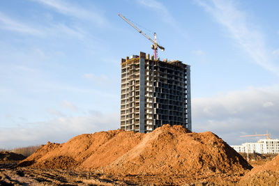 Low angle view of crane by building against sky