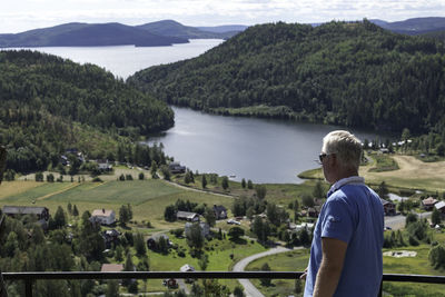 Rear view of man standing by lake against trees