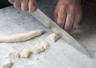 Cropped hands of chef cutting dough on table in commercial kitchen