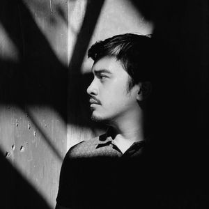 Thoughtful young man standing by wall on sunny day